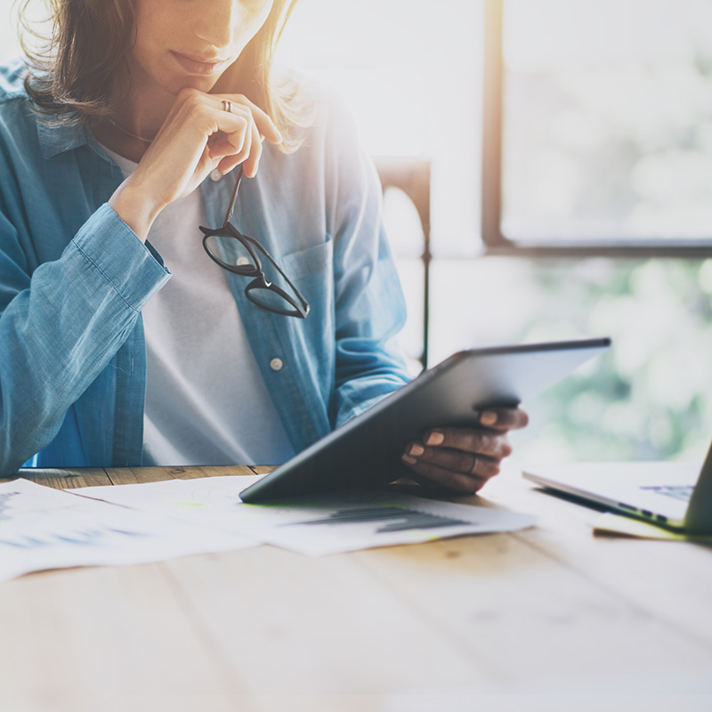 A woman reading sales data on a tablet in a sunny room