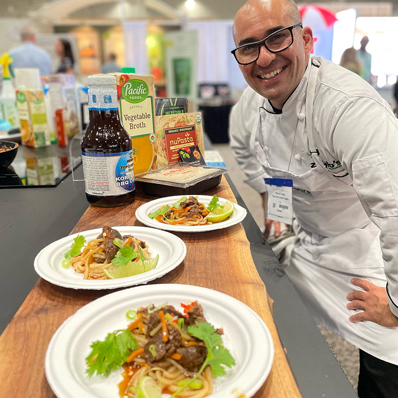 A grinning chef standing proudly over plates of food