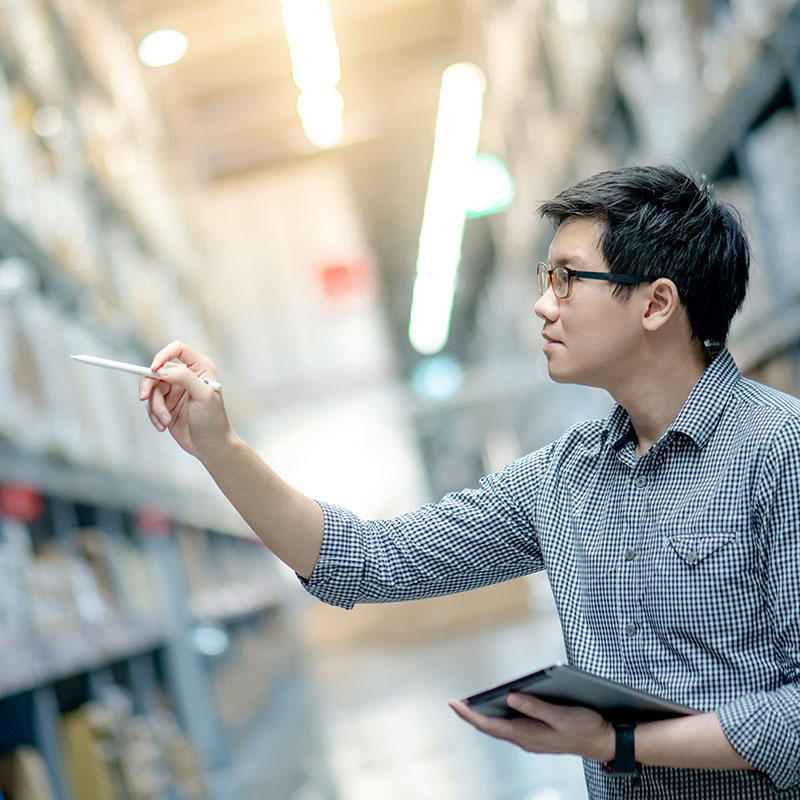 A man wearing glasses and holding a tablet points to a product on a shelf with a stylus