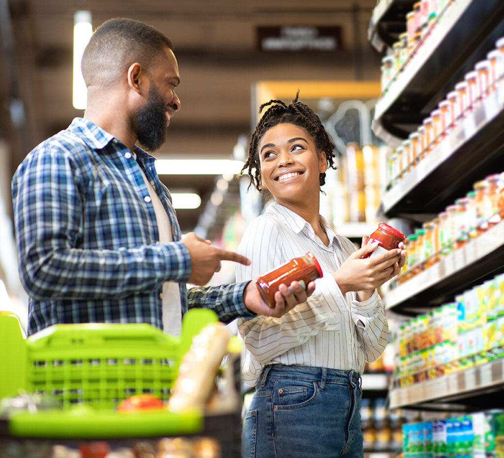 A couple comparing pasta sauces in a grocery aisle